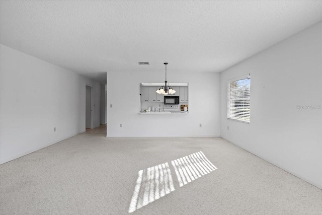 unfurnished living room featuring light carpet, a textured ceiling, and an inviting chandelier