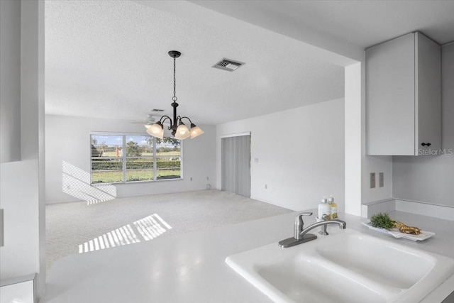 kitchen with an inviting chandelier, a textured ceiling, carpet flooring, pendant lighting, and sink