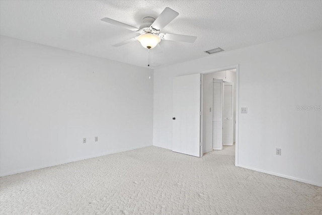 spare room with a textured ceiling, light colored carpet, and ceiling fan