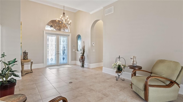 foyer entrance featuring ornamental molding, light tile patterned floors, an inviting chandelier, a towering ceiling, and french doors