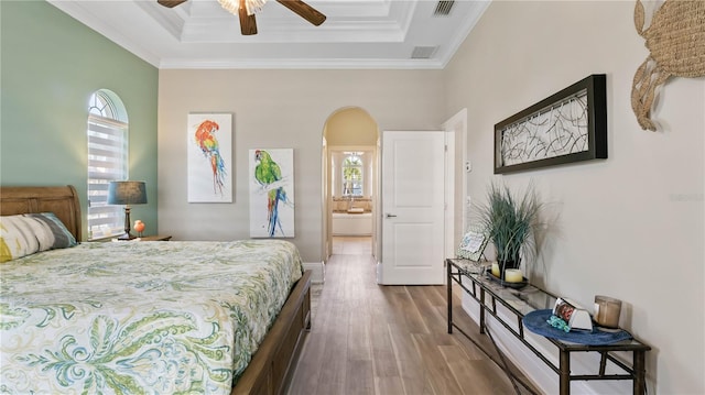 bedroom featuring dark hardwood / wood-style flooring, ensuite bath, ornamental molding, ceiling fan, and a raised ceiling