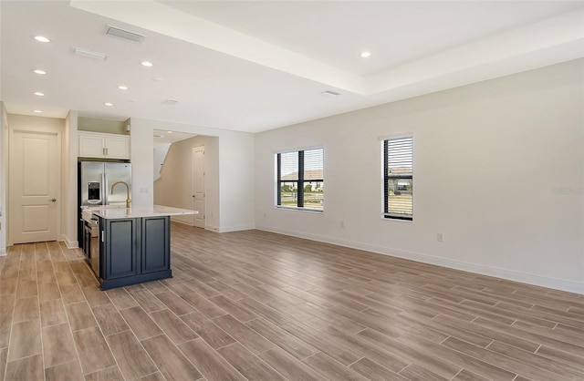 kitchen featuring blue cabinetry, stainless steel fridge, white cabinetry, and a kitchen island with sink