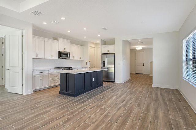 kitchen with white cabinetry, tasteful backsplash, light hardwood / wood-style flooring, an island with sink, and appliances with stainless steel finishes