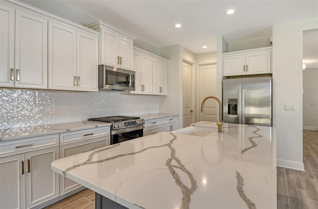 kitchen featuring light stone counters, stainless steel appliances, sink, white cabinets, and a kitchen island