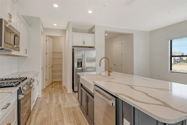 kitchen with light stone countertops, sink, an island with sink, white cabinets, and appliances with stainless steel finishes