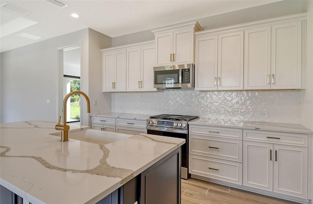 kitchen featuring white cabinets, light stone counters, stainless steel appliances, and a center island with sink