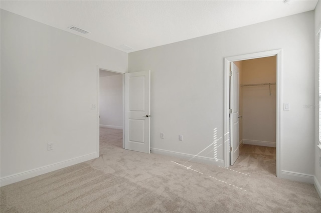 unfurnished bedroom with a spacious closet, a closet, and light colored carpet