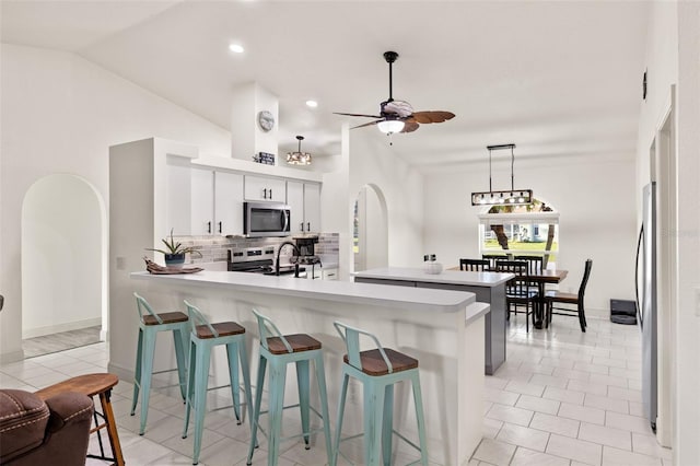 kitchen featuring tasteful backsplash, appliances with stainless steel finishes, kitchen peninsula, white cabinetry, and vaulted ceiling