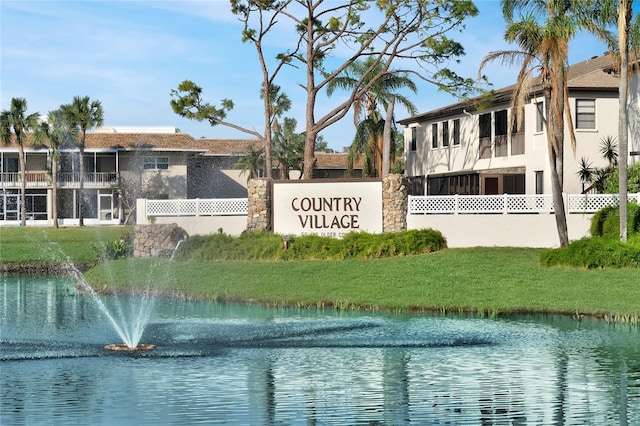 community / neighborhood sign featuring a water view and a lawn