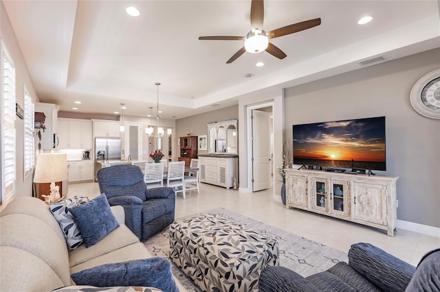 living room featuring a tray ceiling, light tile patterned floors, and ceiling fan with notable chandelier