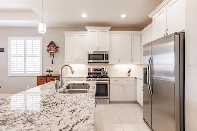 kitchen with light stone countertops, appliances with stainless steel finishes, sink, pendant lighting, and white cabinetry