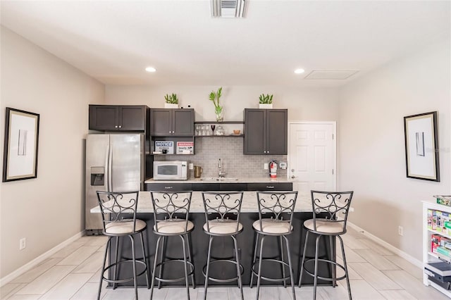 kitchen with sink, a kitchen breakfast bar, stainless steel fridge with ice dispenser, dark brown cabinets, and a kitchen island