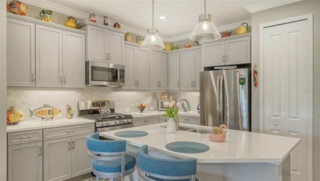 kitchen with pendant lighting, a center island with sink, a kitchen breakfast bar, crown molding, and appliances with stainless steel finishes