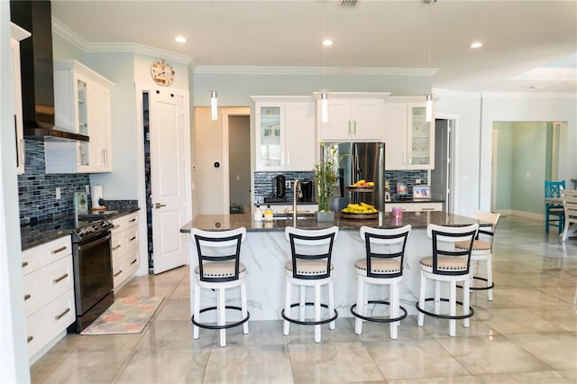 kitchen with black electric range oven, white cabinetry, wall chimney exhaust hood, stainless steel refrigerator, and a center island with sink