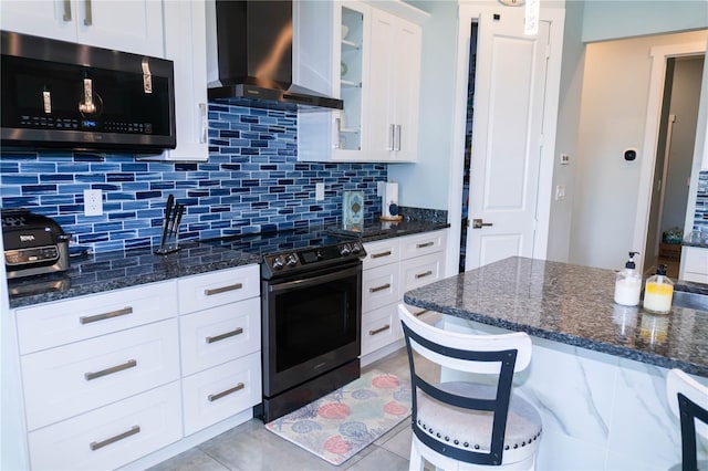 kitchen with white cabinets, decorative backsplash, appliances with stainless steel finishes, dark stone counters, and wall chimney exhaust hood