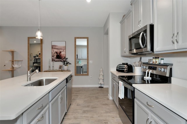 kitchen featuring gray cabinetry, appliances with stainless steel finishes, sink, pendant lighting, and light hardwood / wood-style flooring