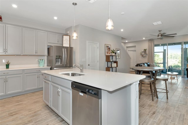 kitchen with sink, ceiling fan, stainless steel appliances, pendant lighting, and a kitchen island with sink