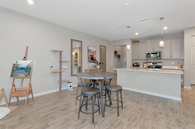 kitchen featuring a kitchen island with sink, light wood-type flooring, pendant lighting, gray cabinetry, and stainless steel appliances