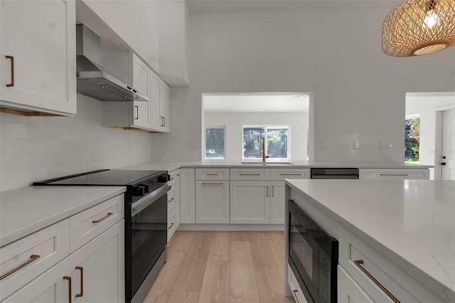 kitchen with wall chimney exhaust hood, black microwave, a healthy amount of sunlight, and stainless steel electric range oven