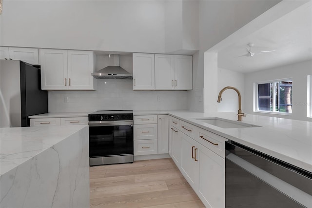 kitchen with white cabinets, appliances with stainless steel finishes, light wood-type flooring, wall chimney exhaust hood, and sink