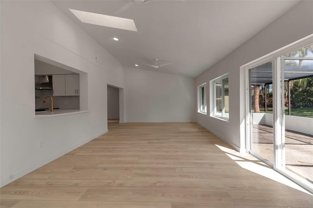 spare room featuring lofted ceiling with skylight, sink, light wood-type flooring, and ceiling fan