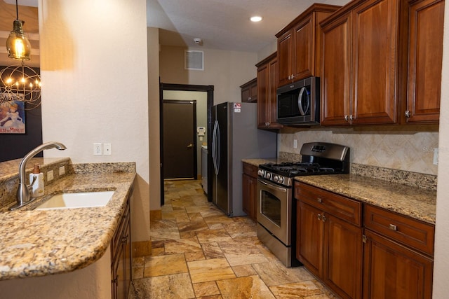 kitchen with pendant lighting, appliances with stainless steel finishes, sink, and light stone countertops