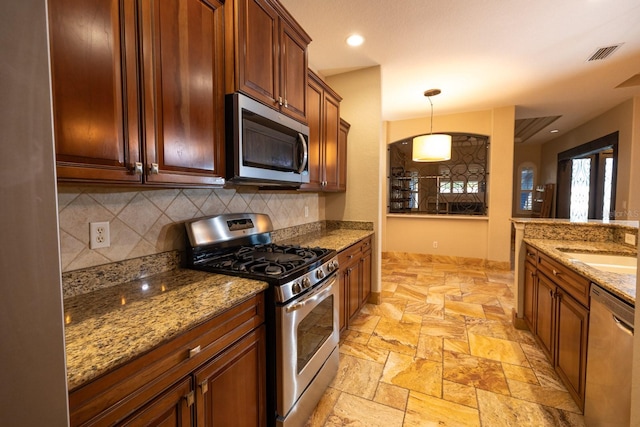 kitchen with stainless steel appliances, sink, light stone countertops, hanging light fixtures, and decorative backsplash