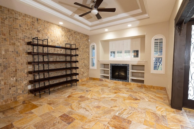 unfurnished living room featuring ceiling fan, a raised ceiling, tile walls, and ornamental molding