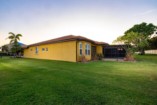 property exterior at dusk featuring a sunroom and a yard