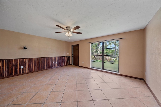 tiled empty room featuring wood walls, a textured ceiling, and ceiling fan