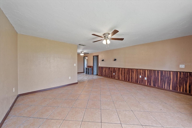 empty room featuring ceiling fan, wood walls, a textured ceiling, and light tile patterned floors