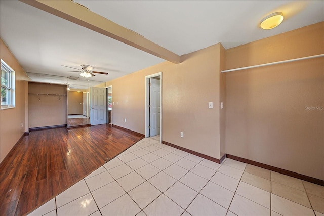 empty room with beamed ceiling, light wood-type flooring, and ceiling fan