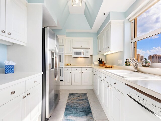 kitchen with white appliances, white cabinetry, lofted ceiling, and sink