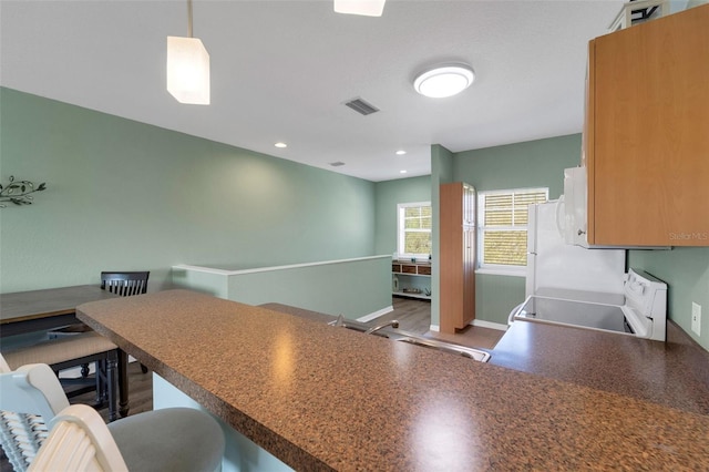 kitchen featuring sink, white range, kitchen peninsula, pendant lighting, and a breakfast bar area