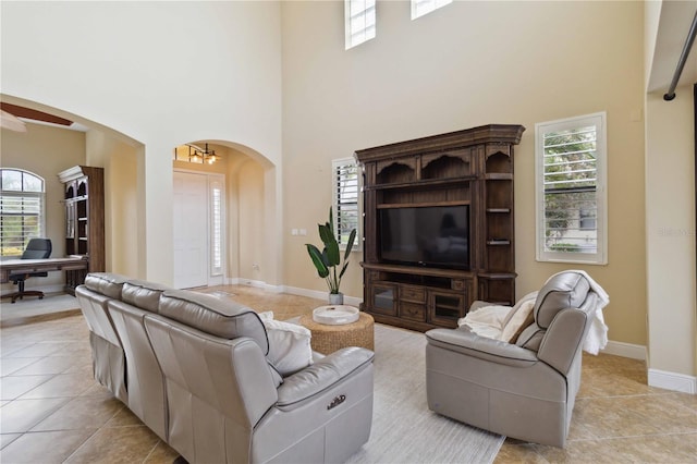 tiled living room with ceiling fan and a high ceiling