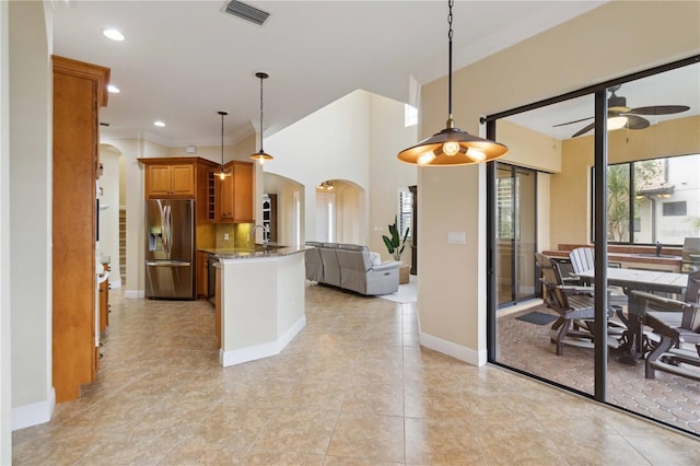 kitchen with stainless steel refrigerator with ice dispenser, hanging light fixtures, light tile patterned floors, ceiling fan, and light stone countertops