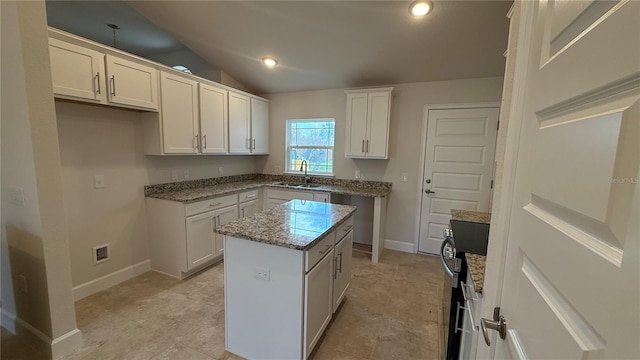 kitchen with lofted ceiling, white cabinets, a kitchen island, light stone countertops, and sink