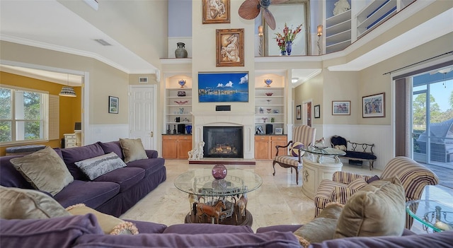 living room featuring a towering ceiling, crown molding, a wealth of natural light, and built in shelves