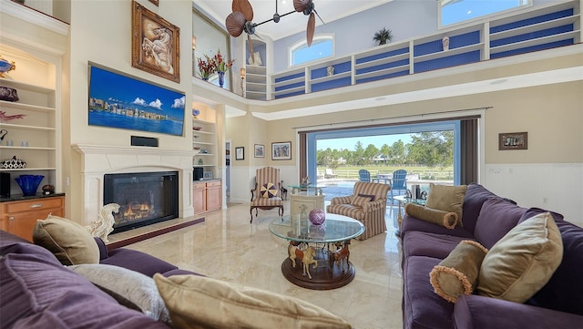 living room featuring ceiling fan, ornamental molding, built in shelves, a towering ceiling, and wooden walls