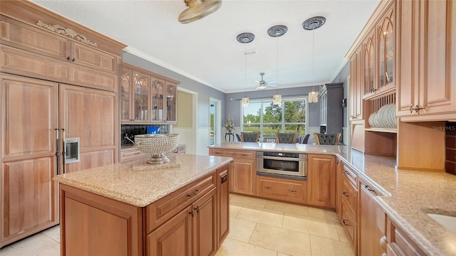 kitchen featuring oven, light stone counters, ornamental molding, decorative light fixtures, and a center island