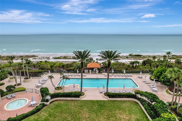 view of pool featuring a water view, a hot tub, a view of the beach, and a patio area