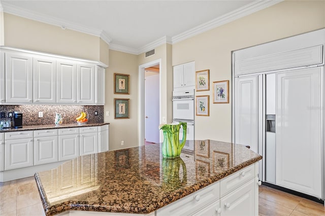 kitchen with white cabinetry, paneled fridge, double oven, and dark stone counters