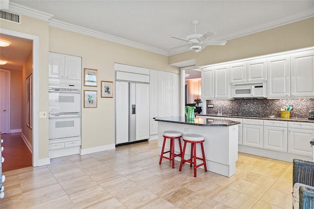 kitchen featuring white appliances, a breakfast bar, a kitchen island, and white cabinets