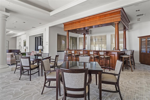 carpeted dining room featuring ornate columns, crown molding, and bar area