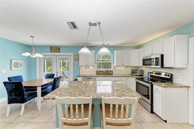 kitchen featuring appliances with stainless steel finishes, white cabinets, a center island, and pendant lighting