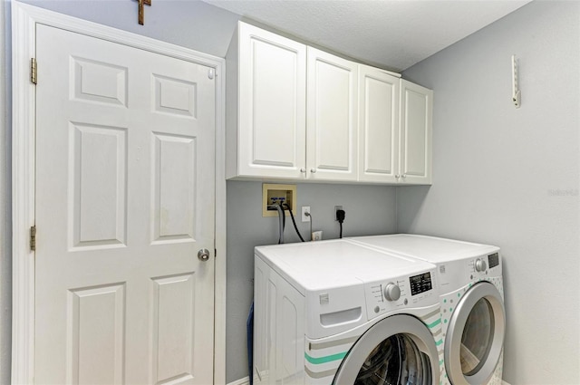 laundry area with washer and dryer, a textured ceiling, and cabinets