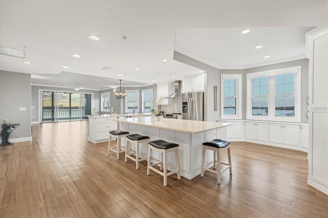 kitchen featuring stainless steel fridge, light wood-type flooring, white cabinetry, and wall chimney exhaust hood