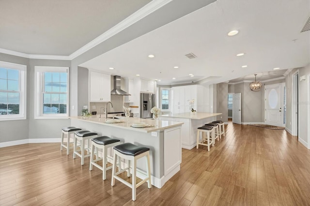 kitchen with white cabinets, stainless steel fridge, wall chimney exhaust hood, and a healthy amount of sunlight