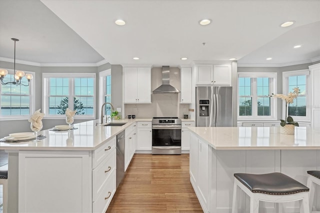 kitchen with pendant lighting, sink, wall chimney exhaust hood, appliances with stainless steel finishes, and a healthy amount of sunlight