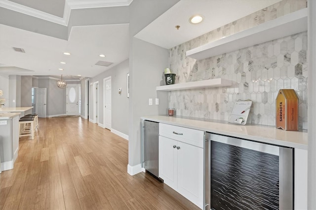 kitchen featuring light wood-type flooring, ornamental molding, beverage cooler, white cabinets, and stainless steel refrigerator